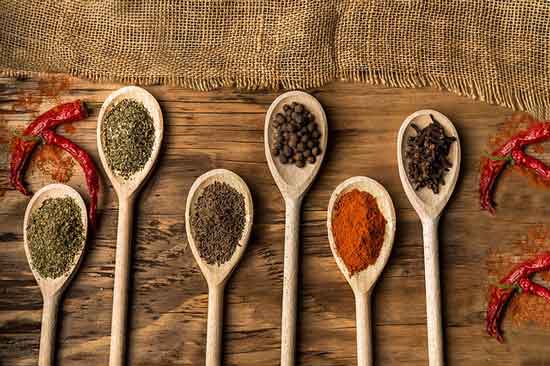 Cuillères en bois alignées sur une table rustique, remplies d'épices variées, dont du poivre noir, des herbes séchées et du piment rouge, illustrant l'élégance et la créativité dans l'Art de la table