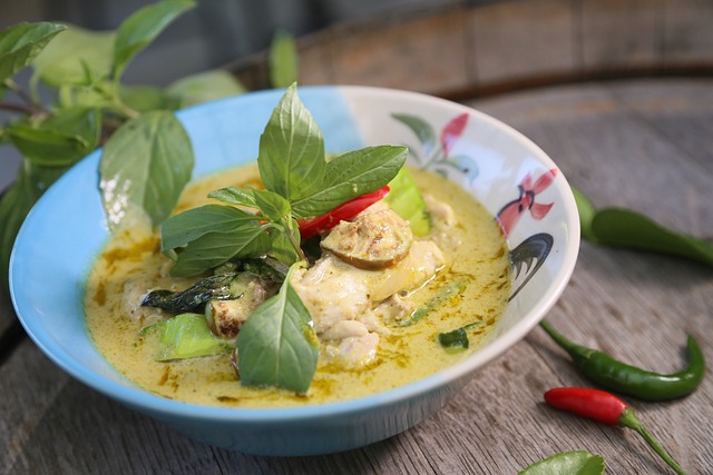 Curry vert thaïlandais servi dans un bol, accompagné de feuilles de basilic frais, de piments rouges et verts, et mettant en valeur le poivre vert en grappes, ingrédient croquant et légèrement piquant caractéristique de la cuisine thaïlandaise.