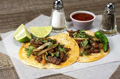 Délicieux tacos de street food avec de la viande grillée, des oignons, de la coriandre, des quartiers de citron vert et de la salsa